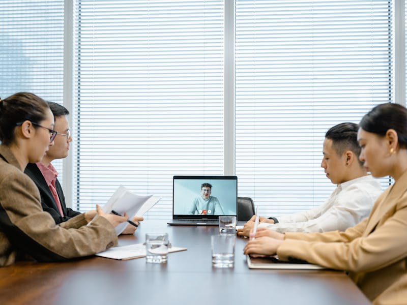 Équipe en salle de réunion connectée à des collègues à distance sur grand écran, illustrant le travail hybride