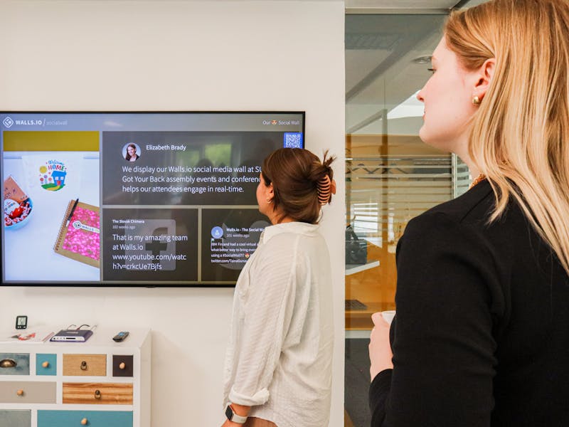Deux collaboratrices découvrant la culture et l'histoire de l'entreprise affichées sur le mur de l'espace de travail